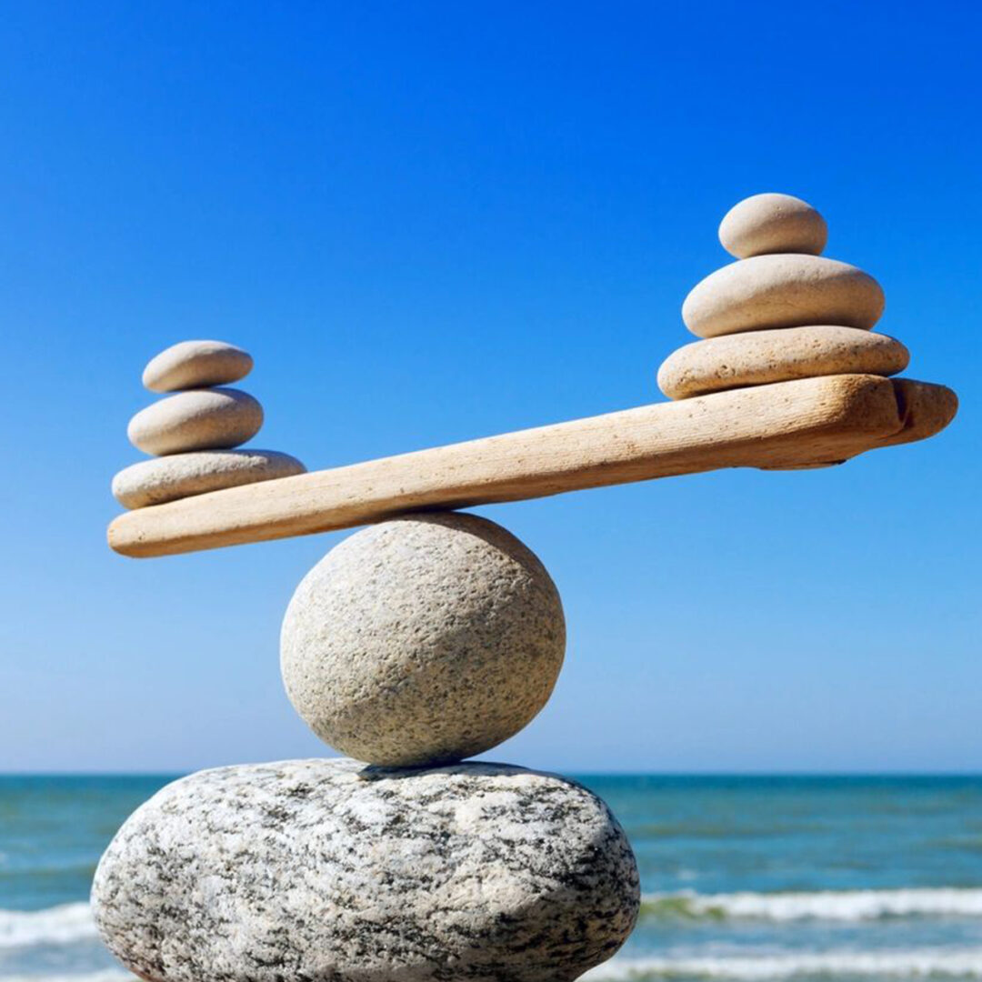 Balanced stones on a beach forming a seesaw over a round stone.