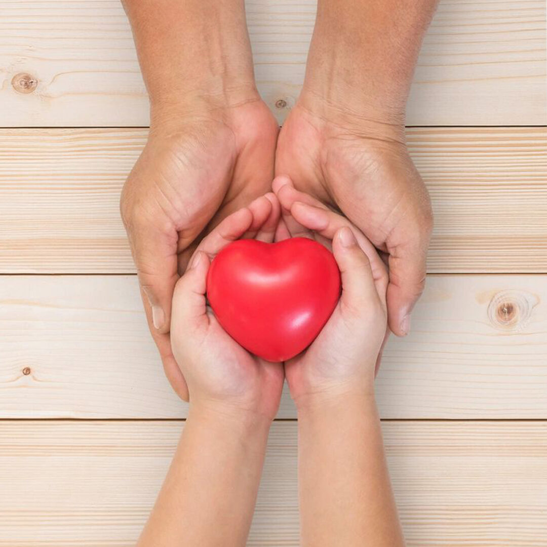 Adult hands holding a child's hands with a red heart.